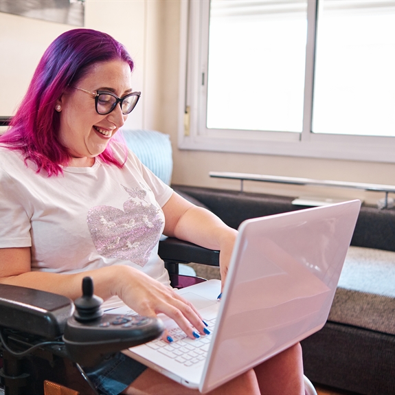 Adult woman with disabilities in a wheelchair working at home with laptop Adult woman with disabilities in a wheelchair working at home with laptop